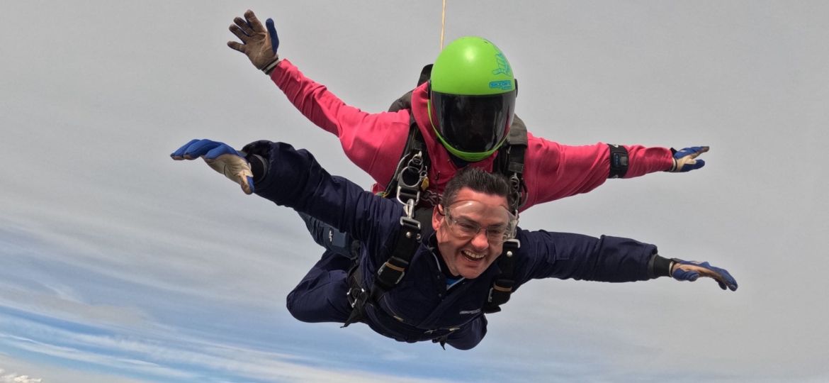 Craig Symonds mid-skydive during a charity jump for the Children’s Bereavement Centre, freefalling through the sky with a huge smile on his face.